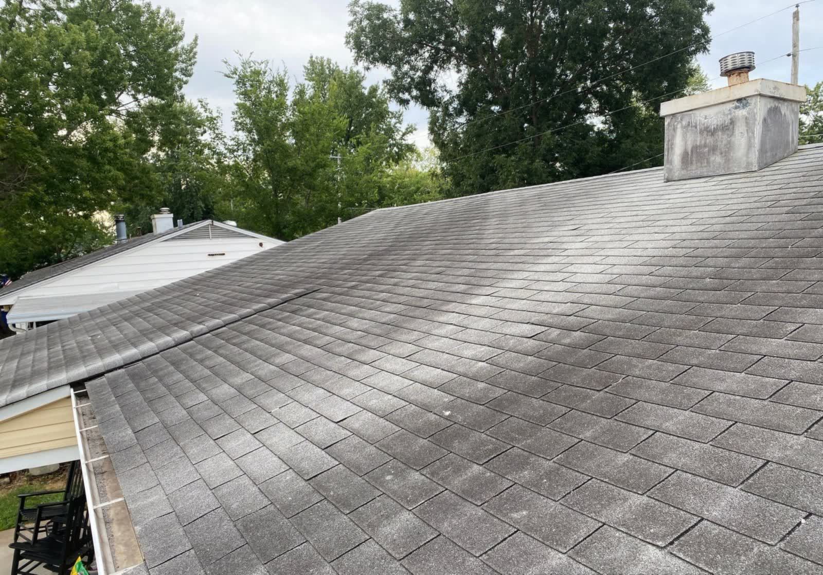 Asphalt shingle roof on a St. Louis-metro home darkened by algae, with a masonry chimney at the ridge
